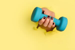 Woman hand holding blue dumbbell on yellow background. Fitness, sport, healthy lifestyle, diet